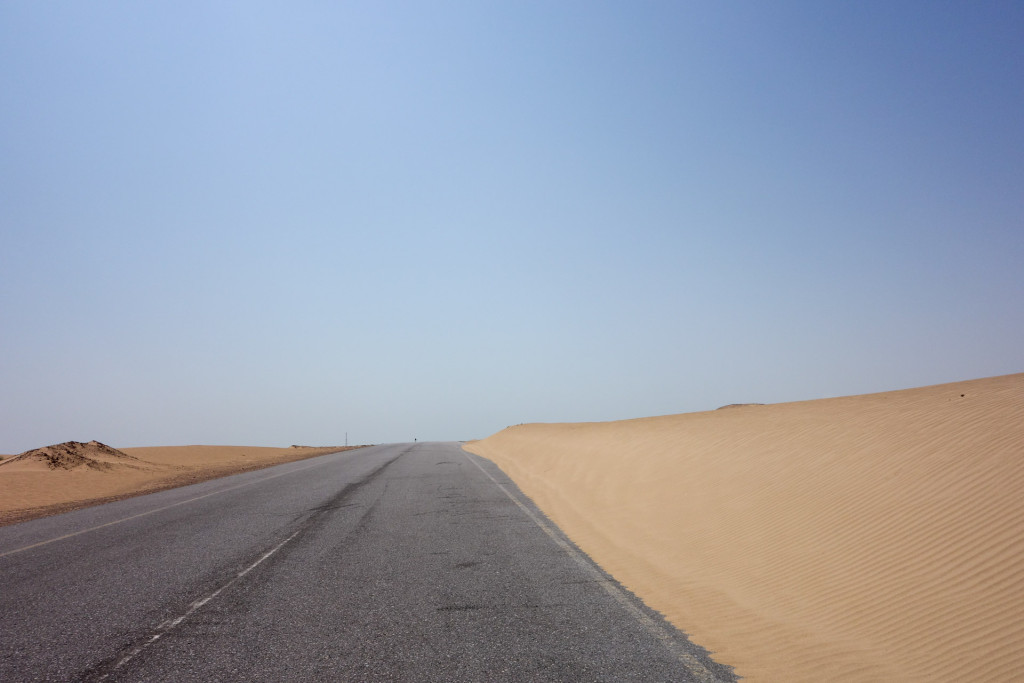 The road is constantly under fire from the sand. The wind blowing from the left and accumulating the sand on the right.